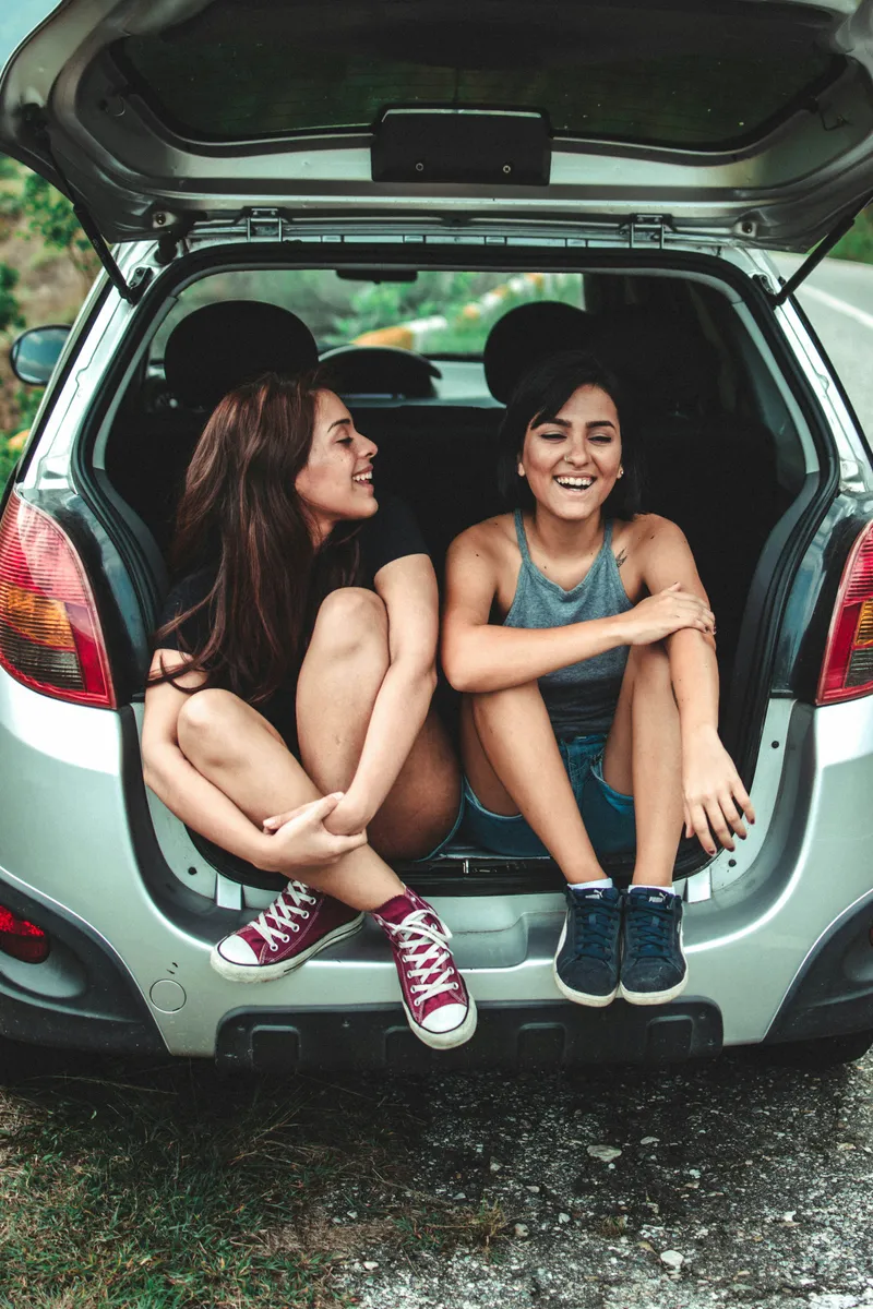 Deux amies complices et souriantes assises dans le coffre d'une voiture